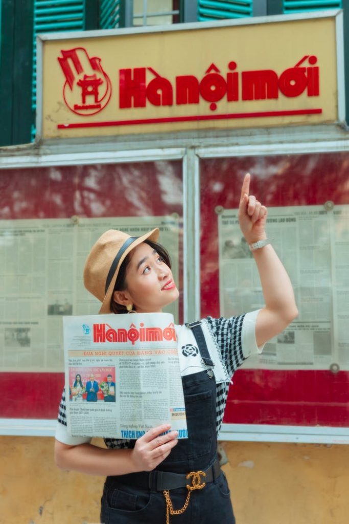 A Woman Pointing Upwards while Holding a Newspaper